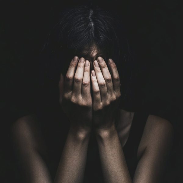 A woman in the dark, hiding her face with her hands.